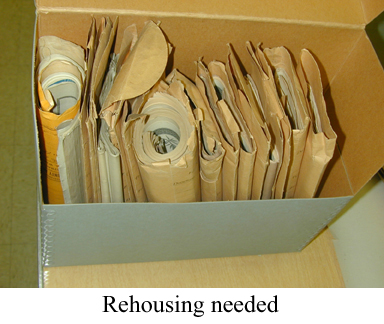 Folded and rolled papers in folders in box with caption "Rehousing needed".