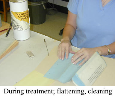 Person's hands on paper with document cleaning powder nearby with caption "During treatment; flattening, cleaning".
