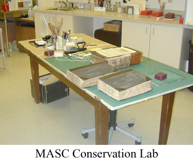 Books and cleaning materials and boxes on table in large room with caption "MASC Conservation Lab"